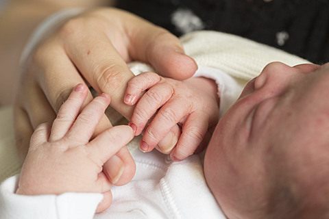 newborn baby holding an adult's finger.