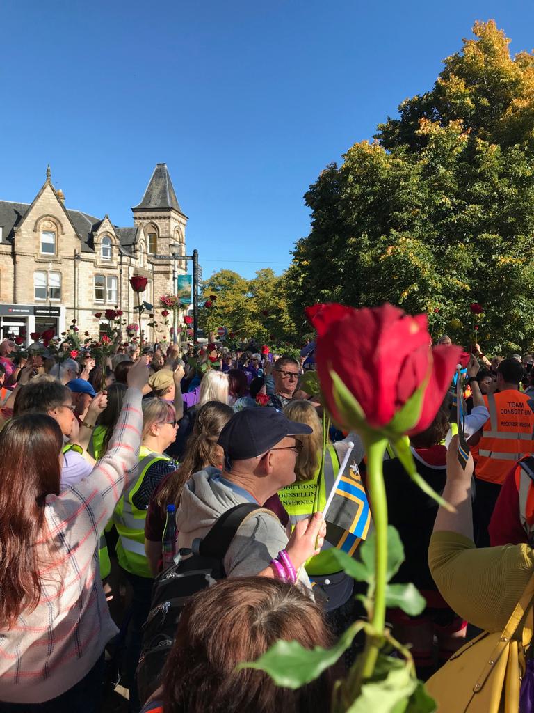 A gathering of people outside Ardross Street with red roses held aloft, one is near the camera.