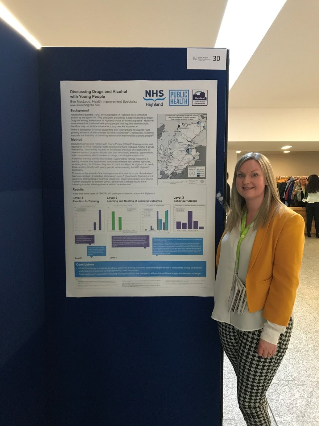 Photo of Health Improvement Specialist, Eve MacLeod standing alongside her poster on 'Discussing Drugs and Alcohol with Young People'.