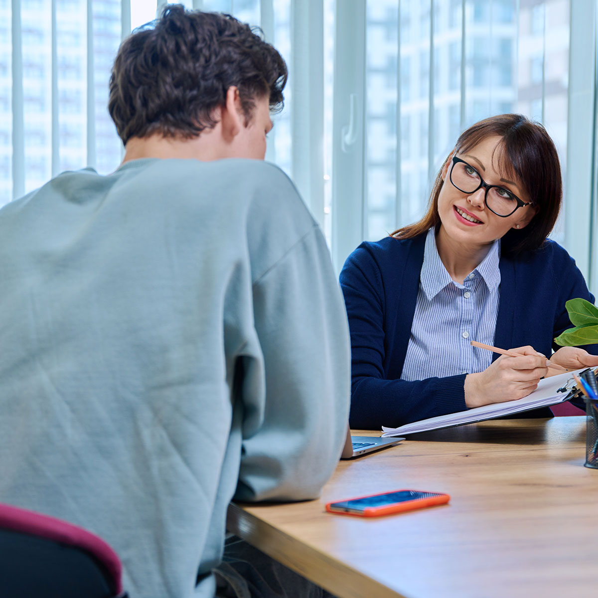 A young man is discussing his mental wellbeing with a female doctor. She is smiling to help him be at ease.