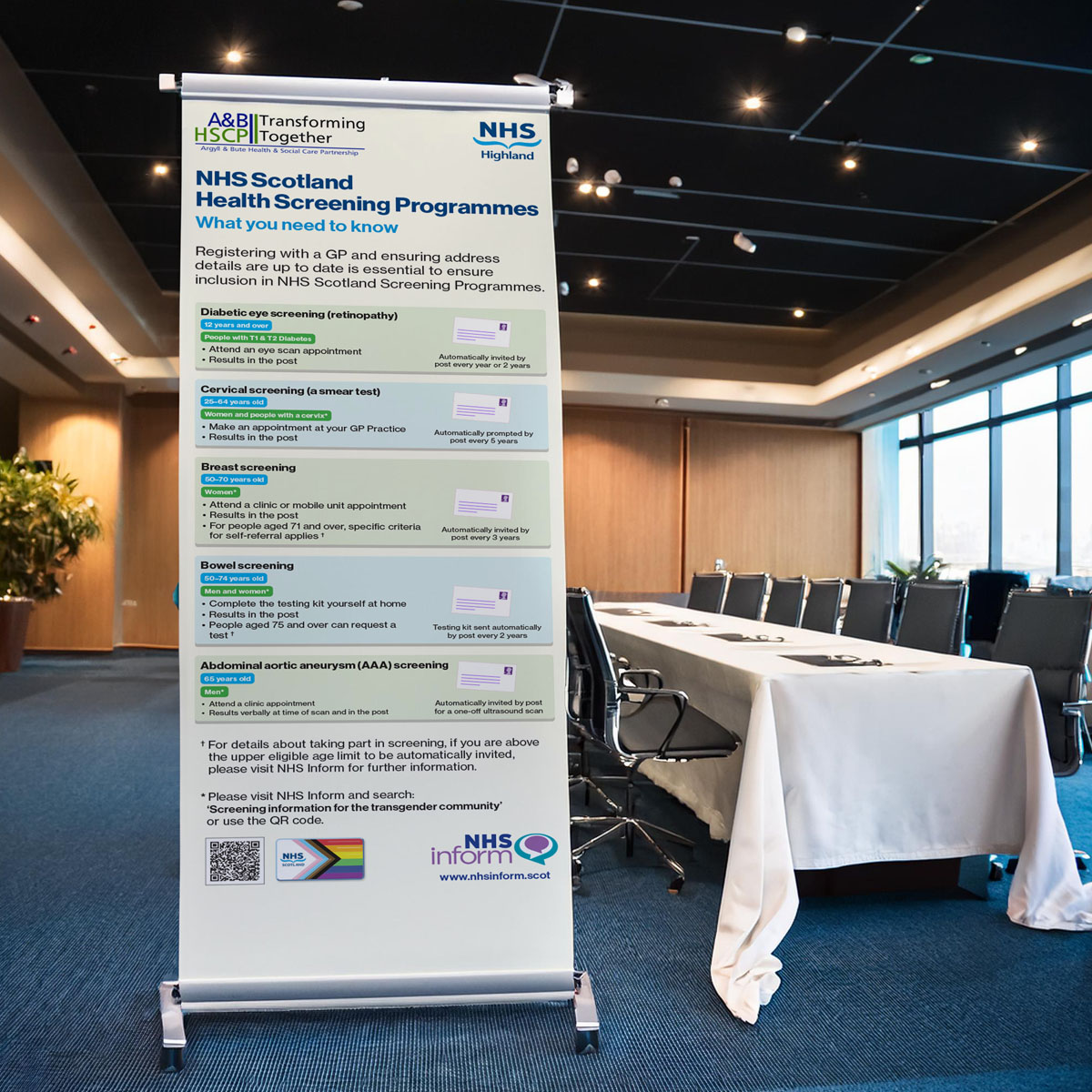 A pull up banner used for screening information is situated in a conference room that is waiting to be used.