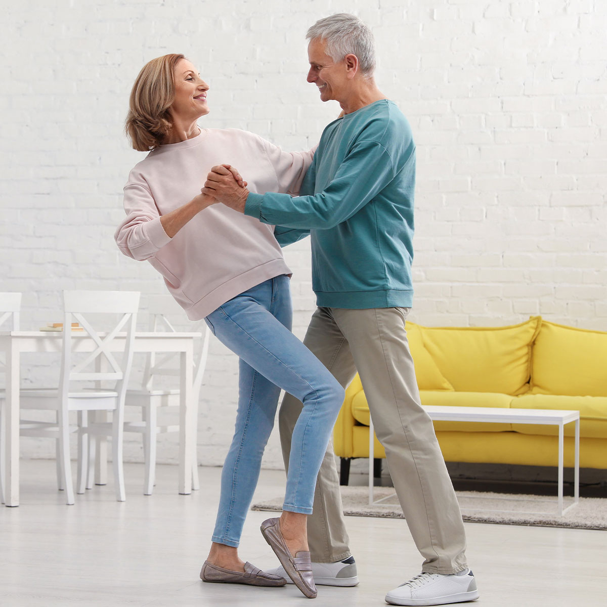 Two older people are in a dancing pose, as if enjoying dancing to some music in their house. The man has slightly dipped the woman as if dancing in a ballroom style.